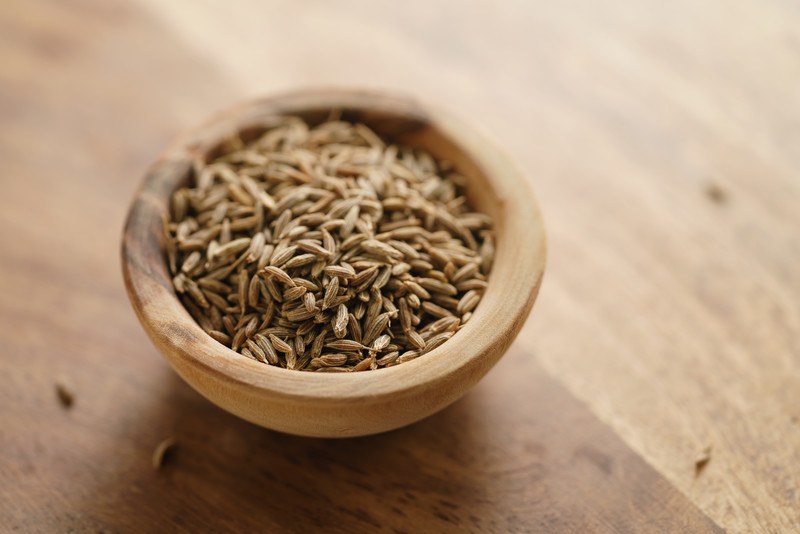 wooden bowl full of cumin seeds resting on a wooden surface