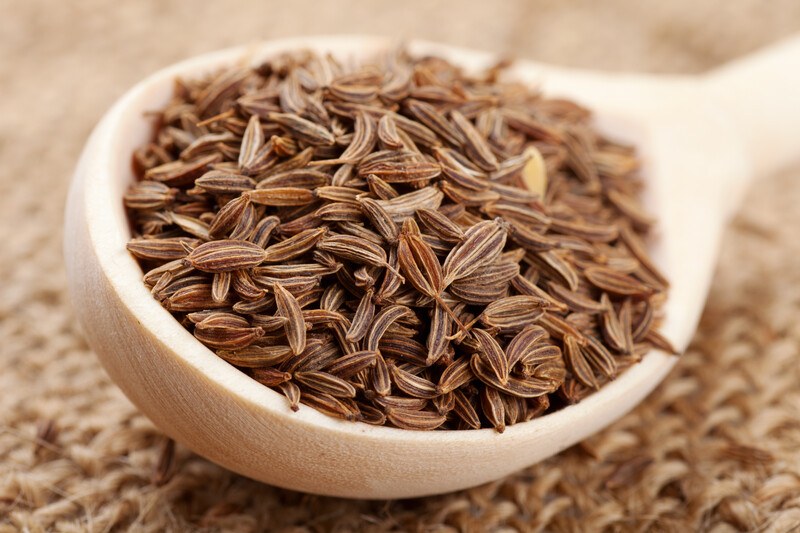 closeup image of a wooden ladle full of cumin seeds