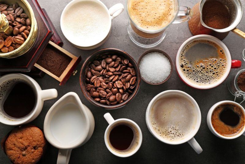 A top down image of various mugs of coffee, along with coffee beans and milk