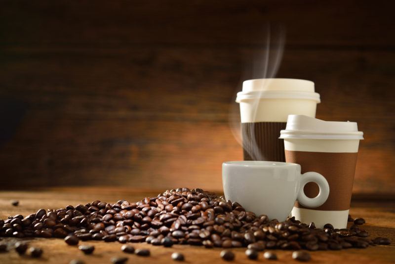 Three different types of coffee cups with steam rising, and coffee beans scattered across a table