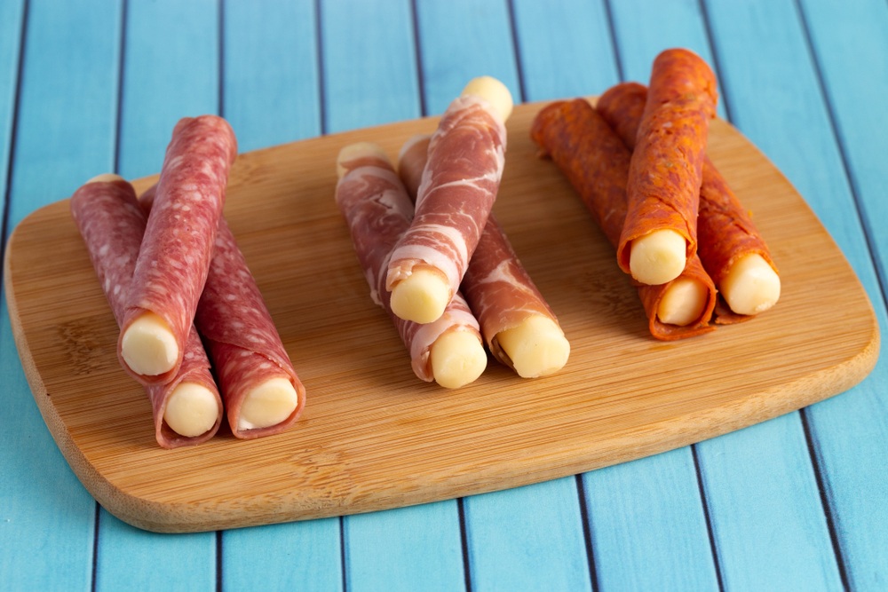 A wooden board with nine mozzarella sticks, which have each been wrapped in cured meat