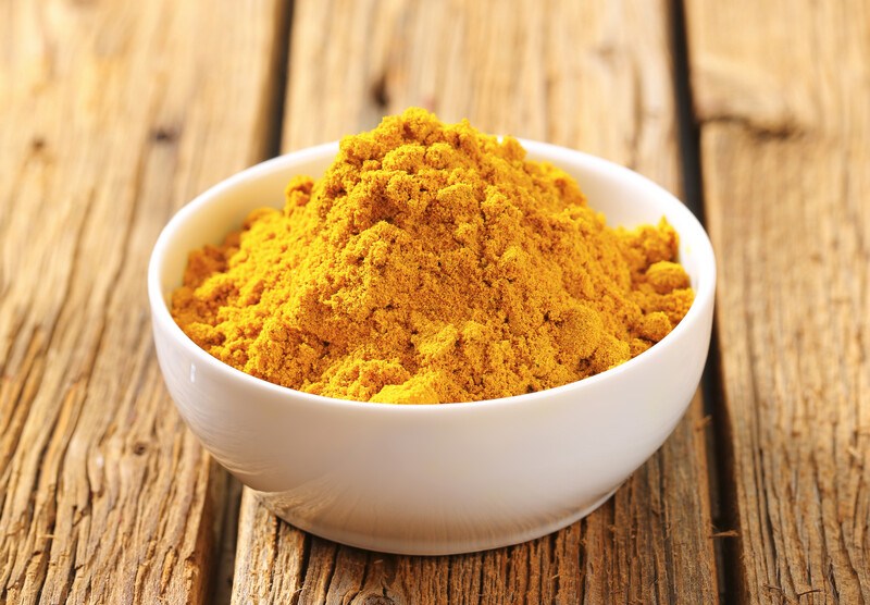 small white bowl with curry powder, resting on a wooden surface