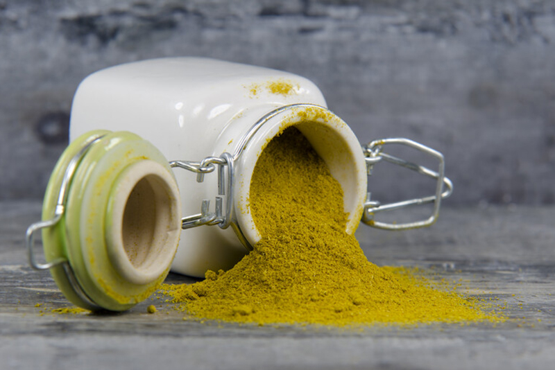 curry powder pouring out of a toppled over cream colored ceramic jar on a natural-colored surface