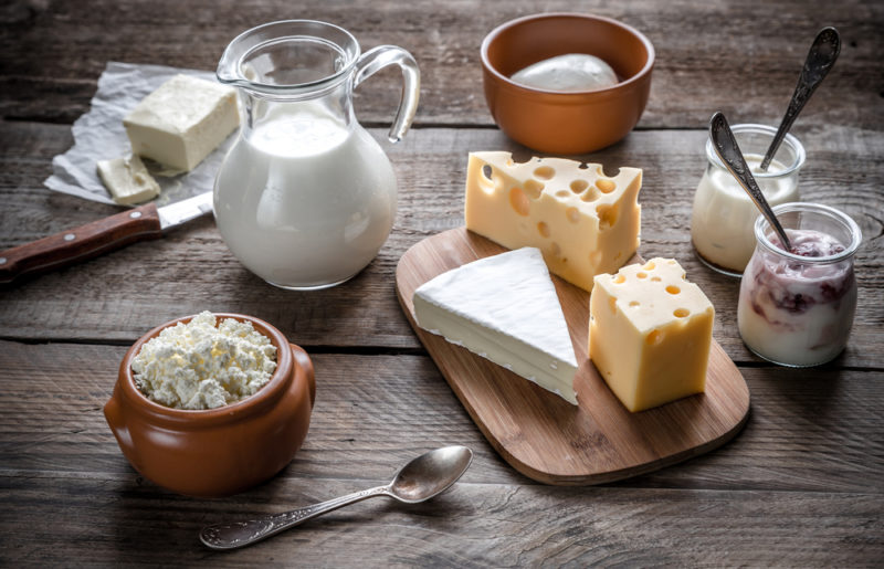 A wooden board with cheese, along with milk, yogurt and various dairy products