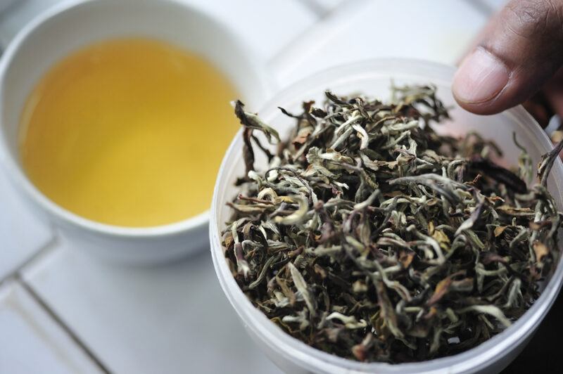 on a tiles surface is a bowl of loose Darjeeling tea with a cup of tea beside it