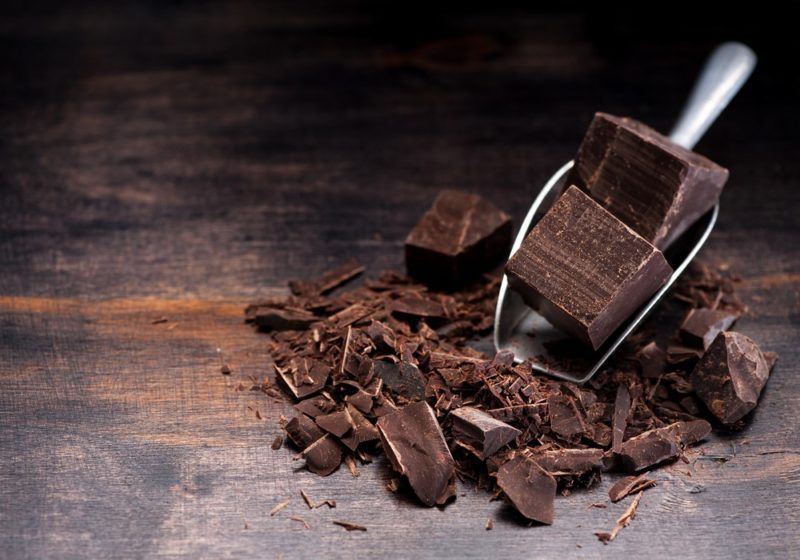 A wooden table with dark chocolate and a metal scoop