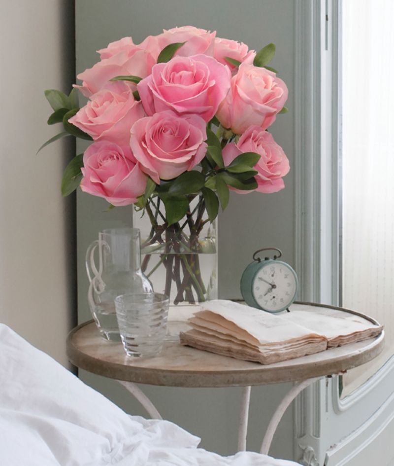 Glass vase with light colored pink roses sitting on the bed side table