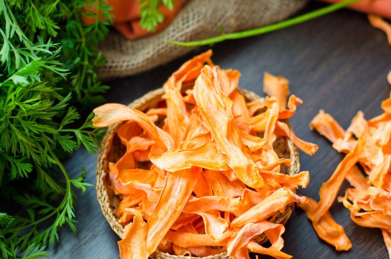 A small bowl of dehydrated carrots next to a brown sack and some greenery