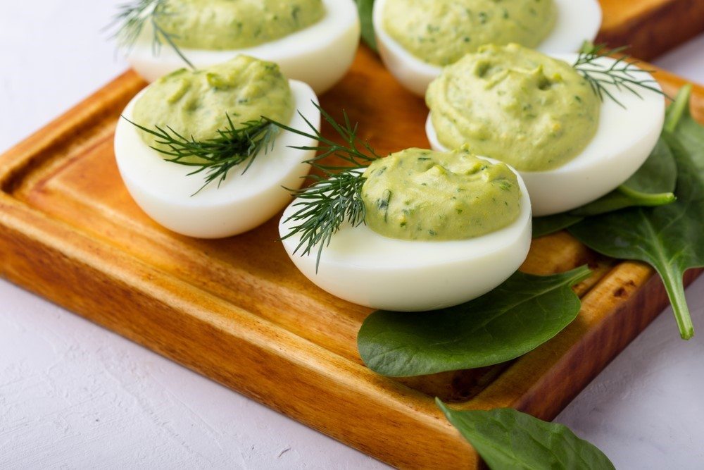 A wooden board with deviled eggs that are made using avocado instead of just egg