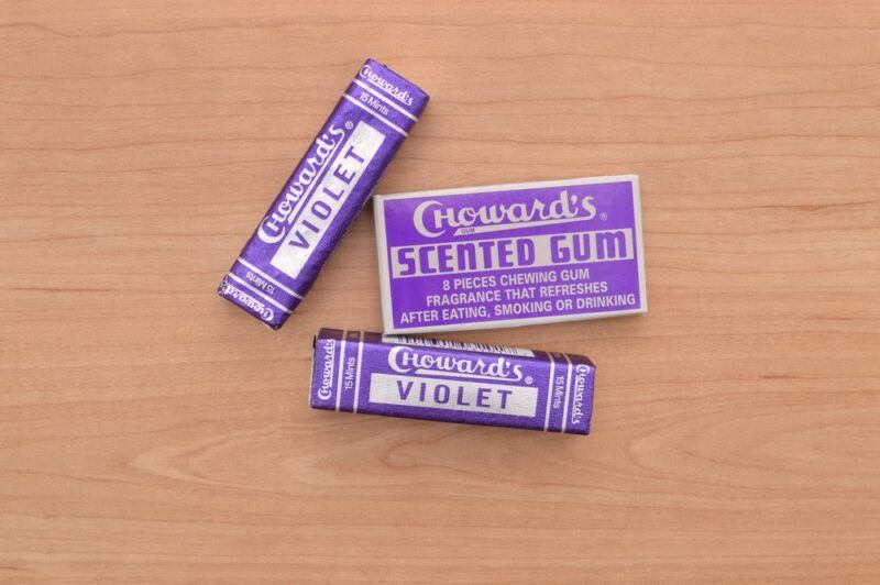 A light wooden table with two purple packets of C. Howard's Violet Mint Candy and a box