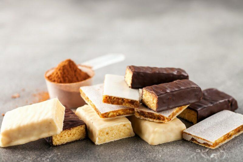 A table with different protein bars and a scoop of protein powder