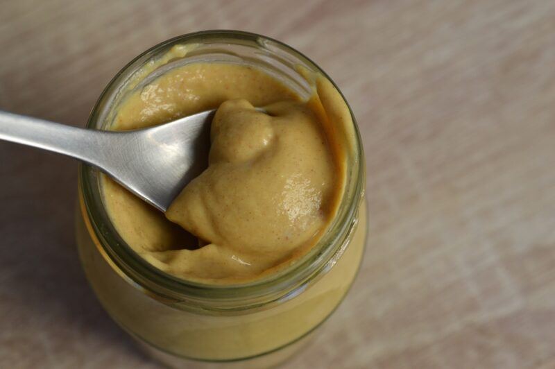 on a wooden surface is an overhead shot of a jar of Dijon mustard with a silver spoon in it