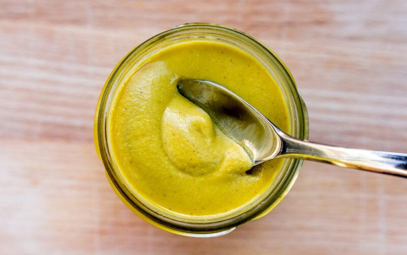 overhead shot of a jar of Dijon mustard with a silver spoon, resting on a wooden surface