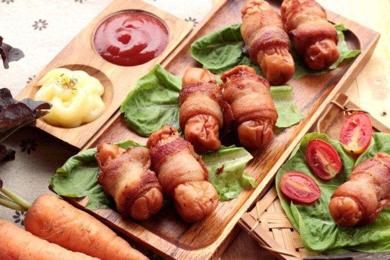 A wooden board with bacon wrapped sausages