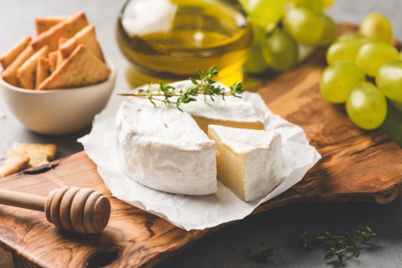 Fresh double cream cheese on a wooden board, with grapes, a honey stick, olive oil, and crackers