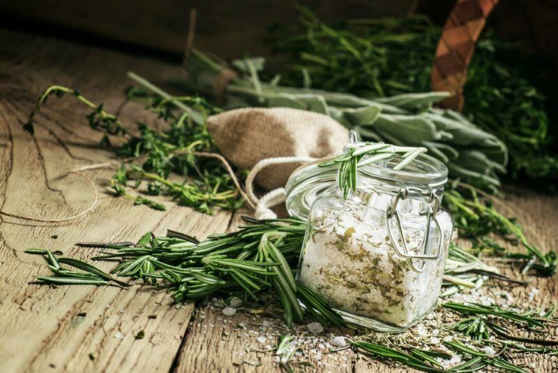 A selection of dried herbs on the table, plus a jar of salt and herbs that's being used as a way to preserve the herbs