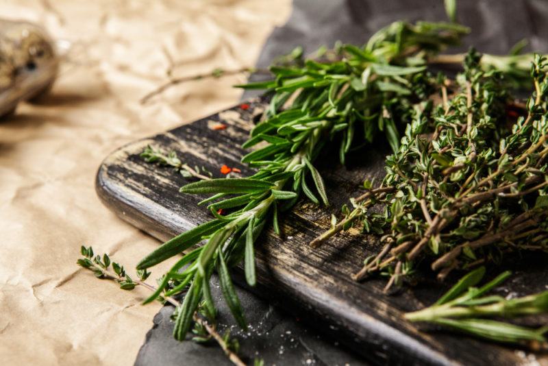 A close up image of a wooden board with dried rosemary and thyme