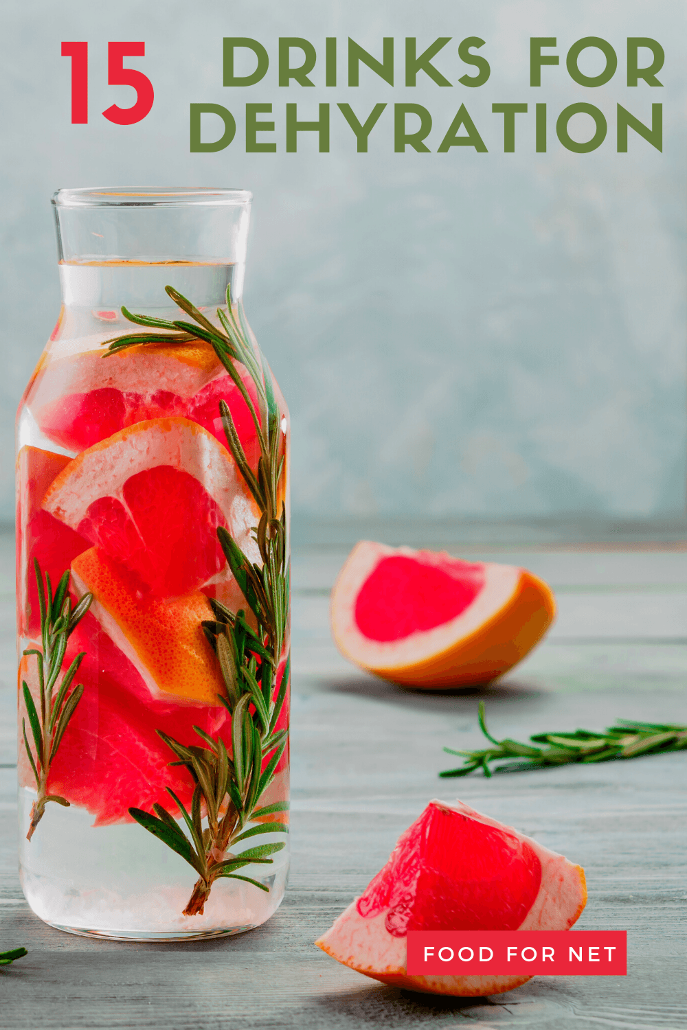 A glass carafe containing grapefruit and rosmary, with grapefruit and rosemary on the table as well