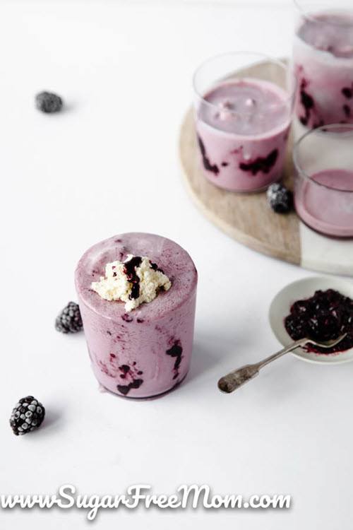 A white table with two glasses of a berry keto smoothie, with some berries scattered on the table as well