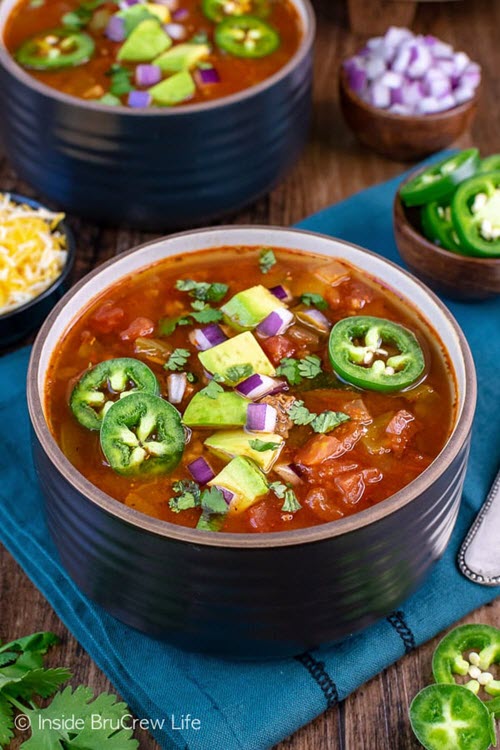 Two black bowls on a table containing chili with avocado and jalapenos
