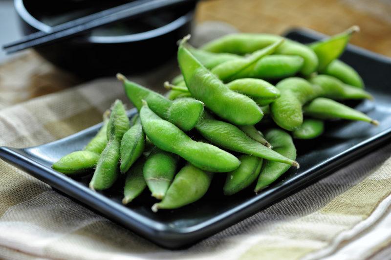 A black plate containing cooked edamame