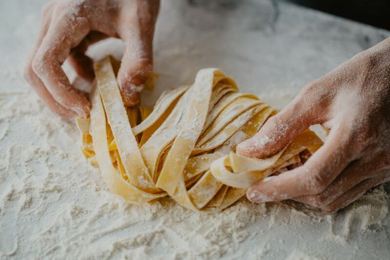 Two hands making fresh egg pasta on a floured surface