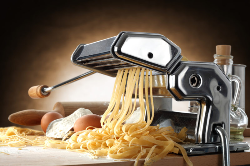 A pasta maker on a table with fressh egg pasta coming out of it