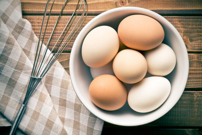 A bowl filled with eggs next to a whisk