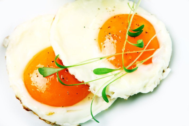 This photo shows an overhead view of two fried eggs with herbs against a white background.