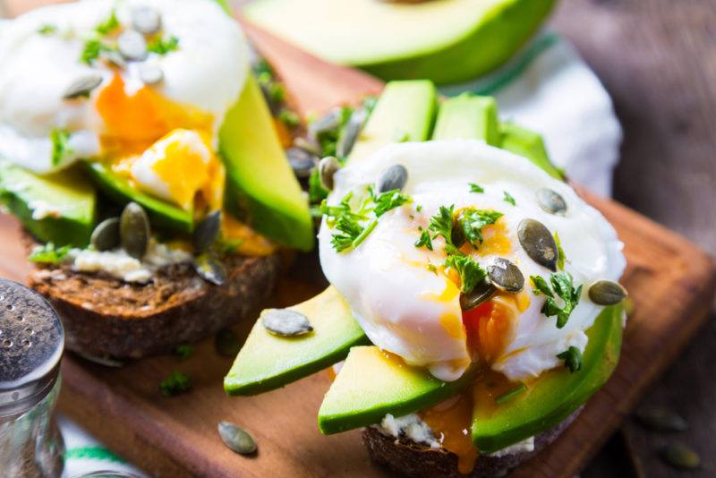 A wooden board with two pieces of toast, sliced avocado and eggs