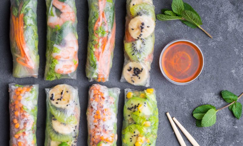 Eight fresh spring rolls on a wooden board next to chopsticks and some sauce