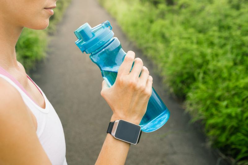 A sportswoman with a bottle of electrolyt water standing on a path outside