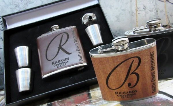 Engraved-Brown-Leather-Flask | Food For Net A dark brown leather flask in a black box and a wood veneer flask on a table.