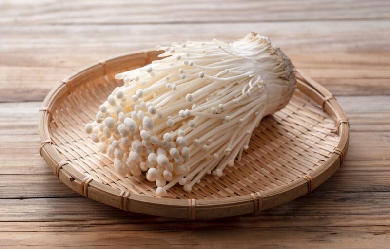 on a wooden surface is a weaved round tray with enoki mushrooms