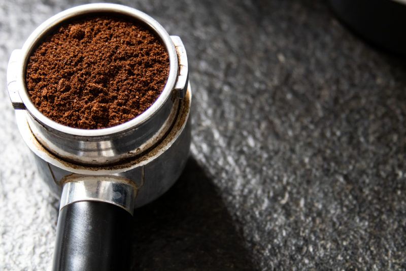 A piece from an espresso machine that contains espresso powder on a table