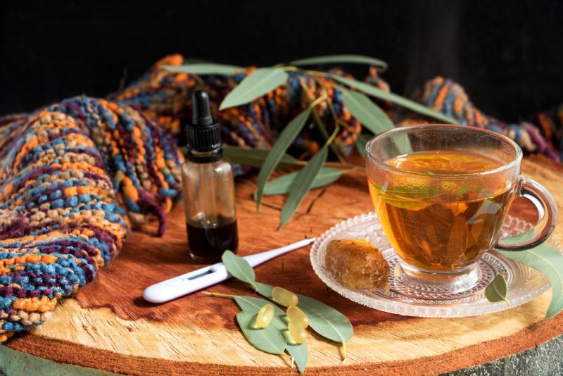 A glass mug of eucalyptus tea with the oil, a scarf and a thermometer