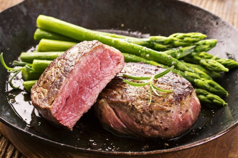 A plate with asparagus spears, next to a whole and a half eye of round steak