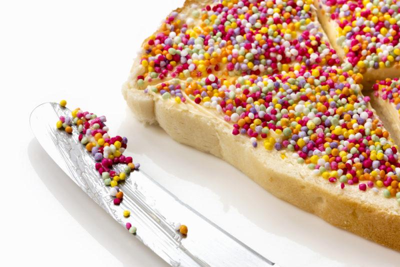 A piece of fairy bread with a knife with sprinkles