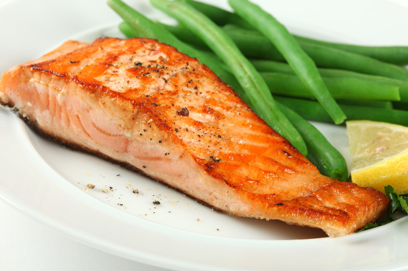 This photo shows a grilled salmon steak, green beans, and a lemon wedge on a white plate.