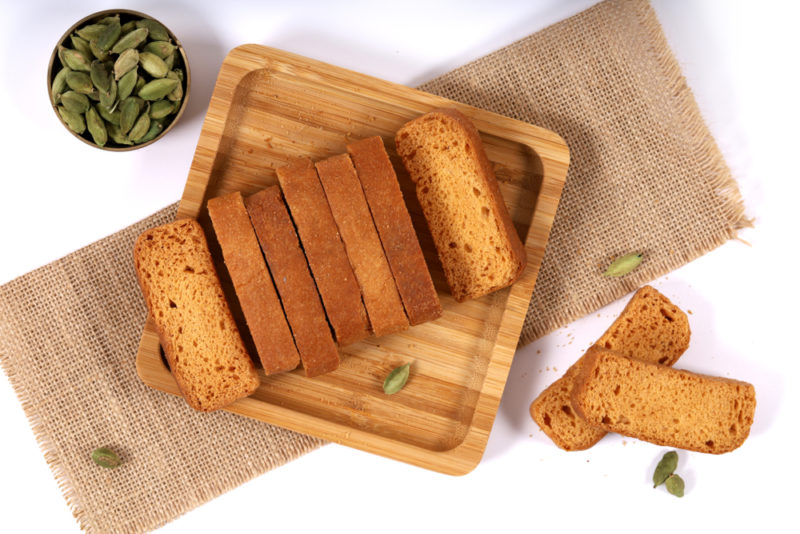 A wooden board with Fette Biscottate and some seeds in a small bowl