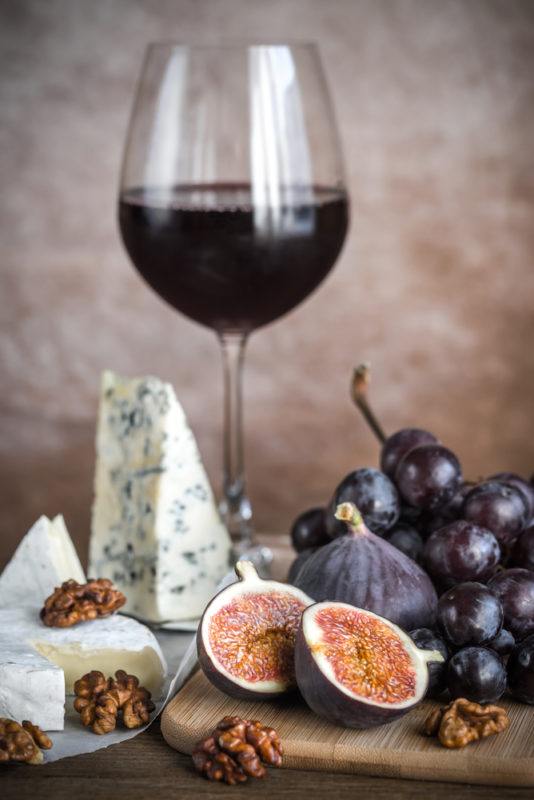 A glass of malbec red wine on a wooden board with blue cheese, walnuts, grapes, and a sliced fig