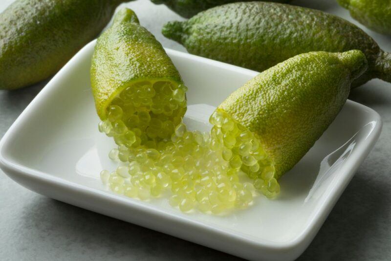 A finger lime on a white plate. It has been cut in half, so the beads of juice can be easily seen