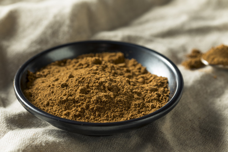 Black ceramic dish with five-spice on a khaki brown cloth, with loose five-spice powder at the back.