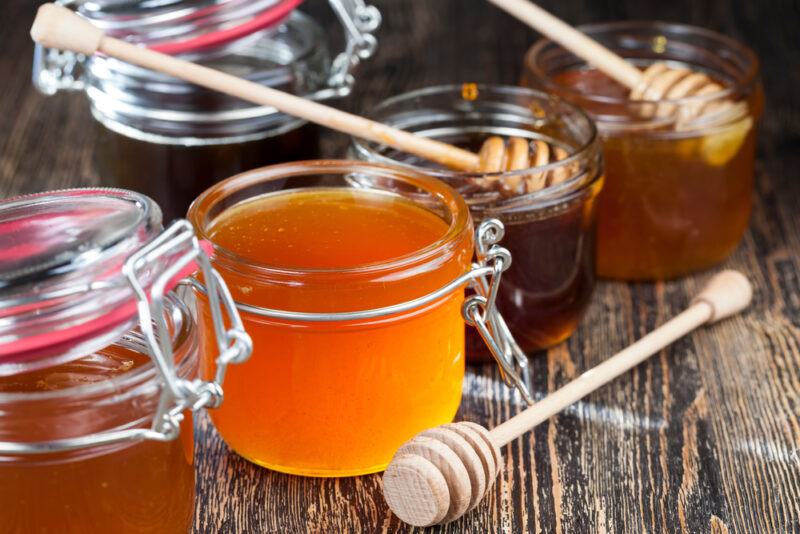 Five different types of honey in jars with stirrers