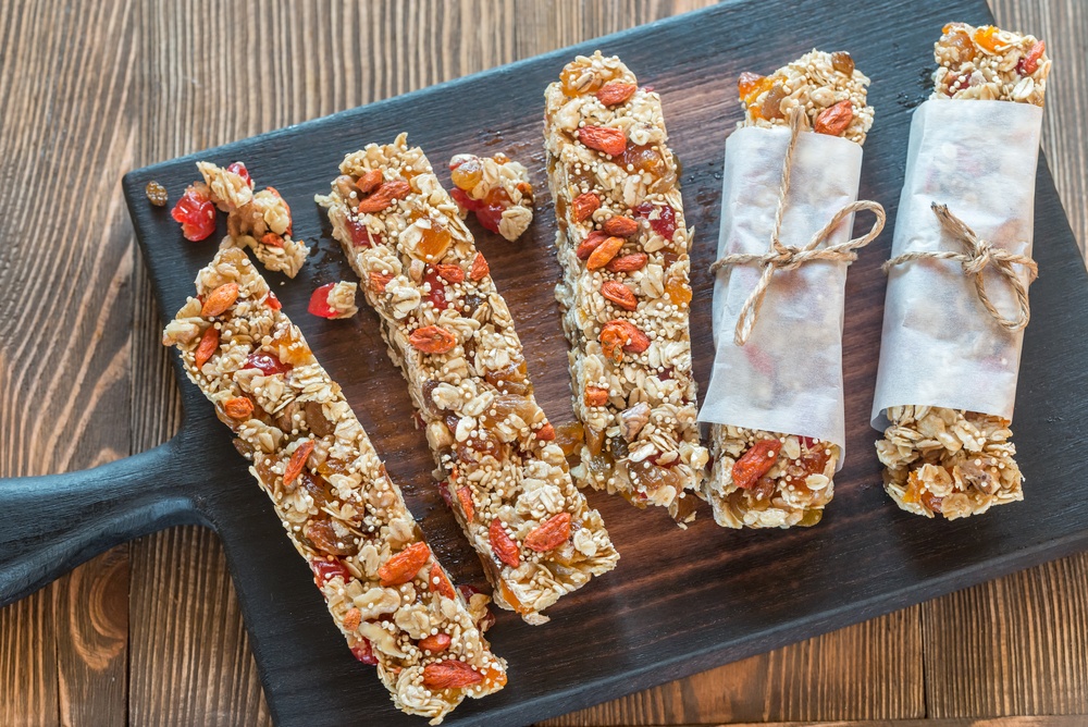 A board with five homemade granola bars, two of which are wrapped in paper