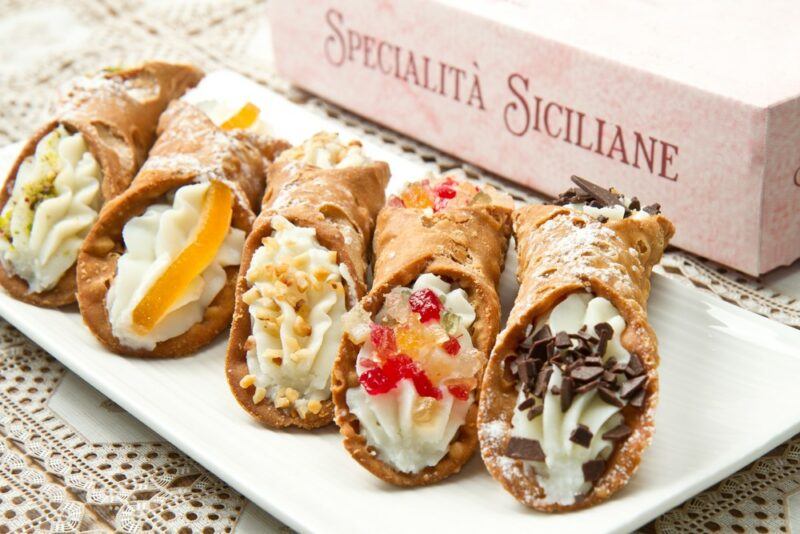 A rectangular white plate containing pieces of Italian cannoli, each with a different type of garnish, including nuts and chocolate chips