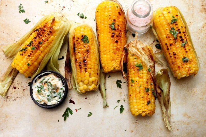 A light colored table with five pieces of grilled corn on top