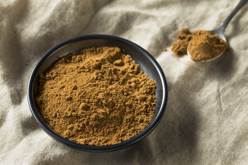 black ceramic bowl with five-spice powder resting on a tan-colored cloth with a spoonful of five-spice beside it