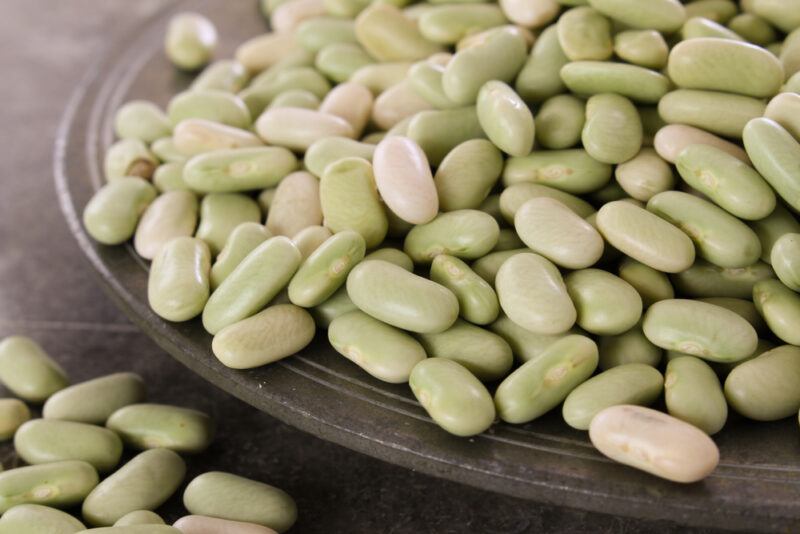 a closeup image of a black dish with flageolet beans with loose flageolet beans beside it