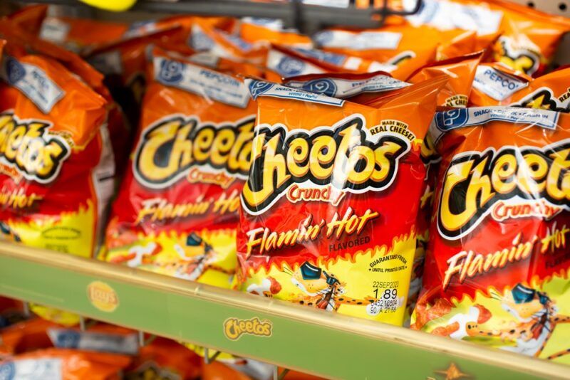 A large number of orange and yellow bags of Flamin' Hot Cheetos on a grocery store shelf.